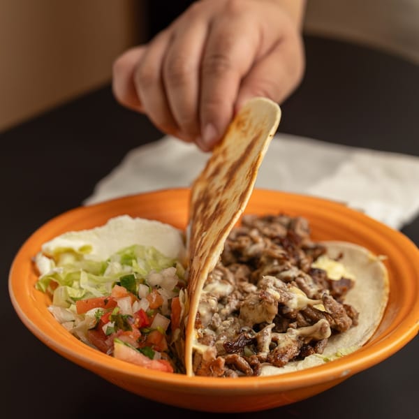 Hand holding a tortilla over a plate of Los Mariachis tacos with meat, cheese, lettuce, and pico de gallo.