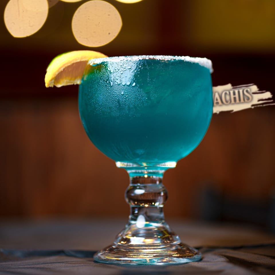 A vibrant blue margarita in a goblet glass, garnished with a lime wedge and salt rim.