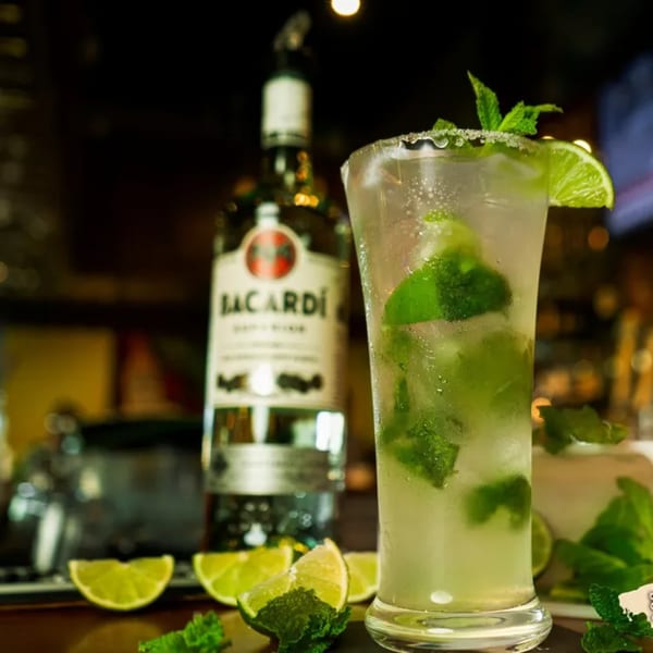A refreshing mojito with lime and mint, next to a Bacardi bottle on a dark bar.