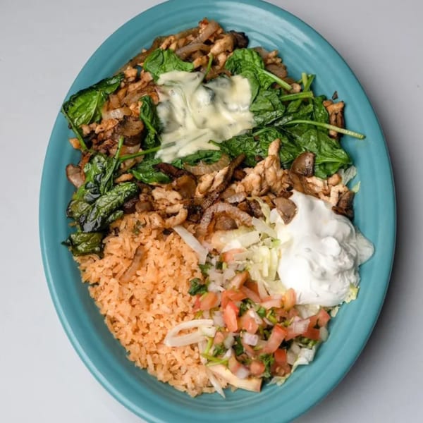 A vibrant Mexican dish with chicken, spinach, rice, pico de gallo, and sour cream on a blue plate.