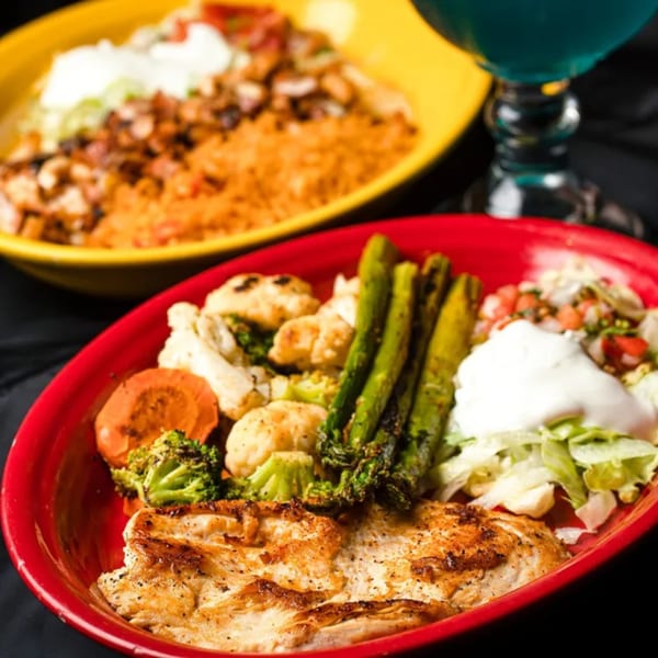 Grilled chicken with roasted vegetables, lettuce, sour cream, and pico de gallo in a red bowl.