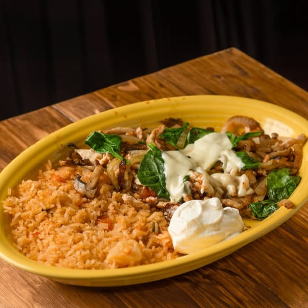 Mexican dish with rice, chicken, spinach, onions, mushrooms, and sour cream on a yellow plate.