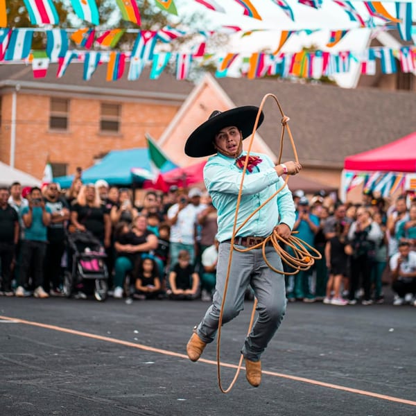 A man in a sombrero and light blue shirt jumps while twirling a rope at a Mexican festival.