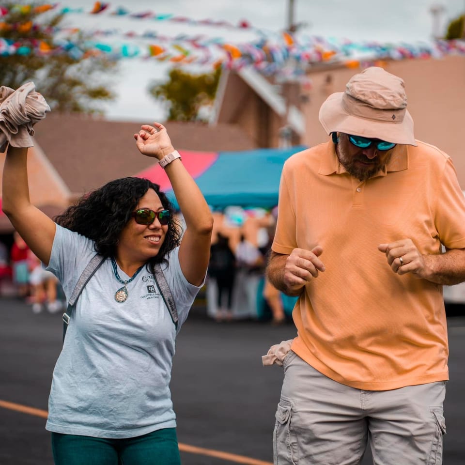 Two people dancing outdoors under colorful banners, celebrating at a Los Mariachis event.