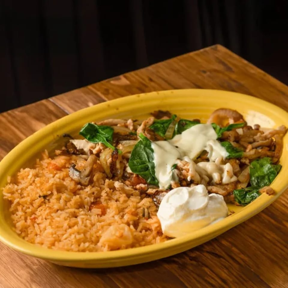 A yellow plate of Mexican rice, chicken, spinach, and sour cream on a wooden table.