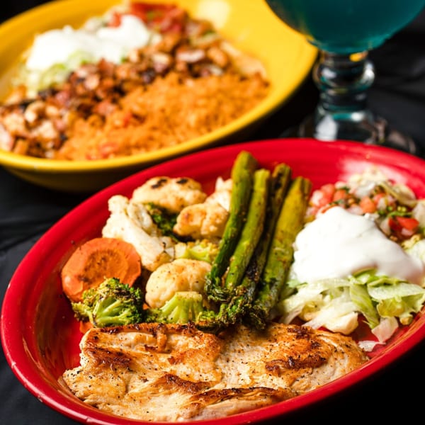 Grilled chicken with roasted vegetables, lettuce, pico de gallo, and sour cream in a red bowl.