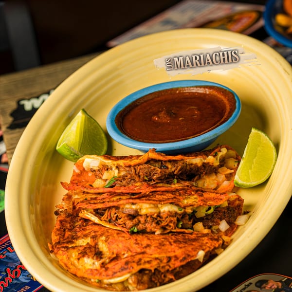 Los Mariachis birria tacos with lime wedges and a side of consommé on a yellow plate.